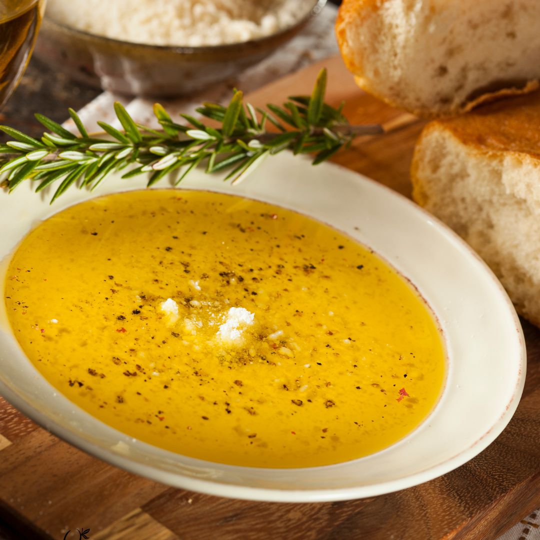 A shallow white bowl of golden extra virgin olive oil seasoned with grated Parmesan cheese, minced garlic, herbs, and red pepper flakes.