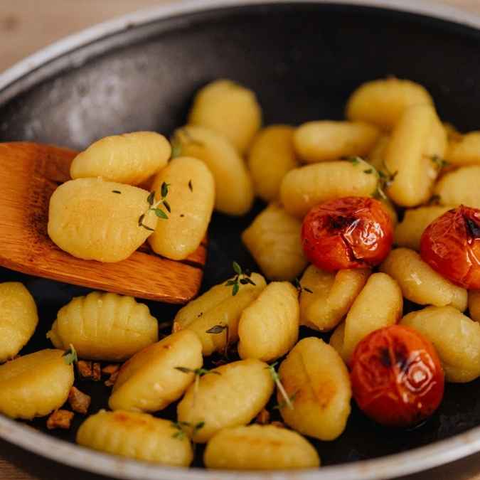 A dark skillet filled with golden, crispy pan-fried gnocchi, burst cherry tomatoes, and fresh thyme sprigs.