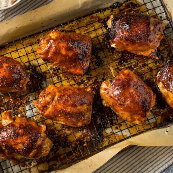 Several deeply browned, glazed chicken thighs resting on a wire baking rack over a lined pan.