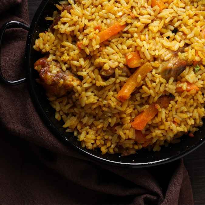 A skillet of warm, golden summer rice cooked with diced carrots and onions, finished with a drizzle of garlic olive oil and honey ginger balsamic.