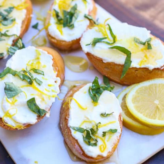 This lemon ricotta bruschetta is made with a creamy citrus ricotta cheese blend topped with extra virgin olive oil, sweet local honey, fresh basil, bright lemon zest, and crunchy salt.