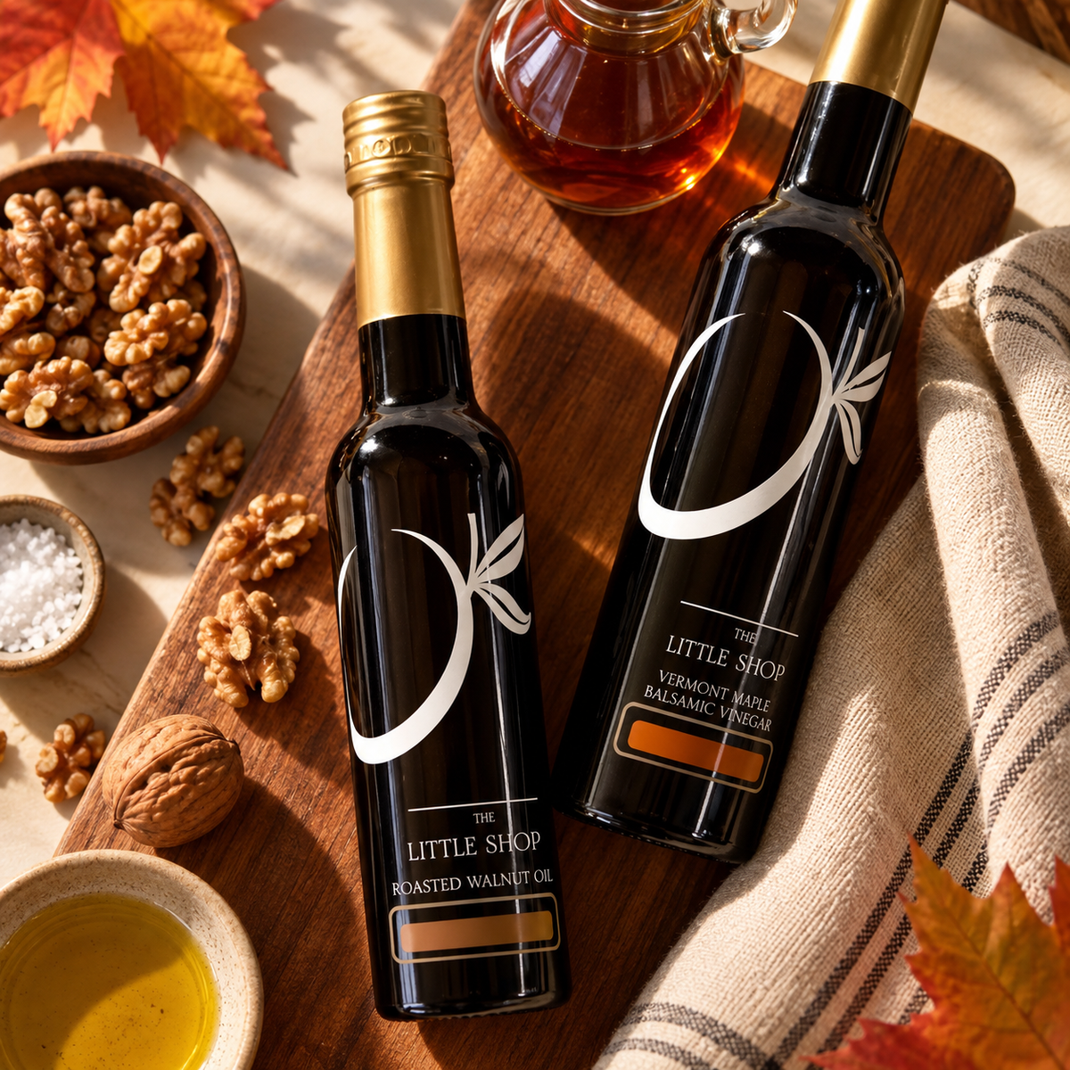 Roasted walnut oil and Vermont maple dark balsamic vinegar bottles from The Little Shop of Olive Oils with walnuts and autumn leaves.