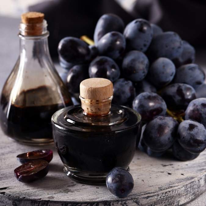 Bottles of aged balsamic vinegar on a rustic table with a bunch of fresh large dark red grapes.