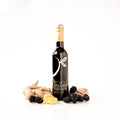 A bottle of gourmet balsamic vinegar by 'The Little Shop' is displayed on a white background, styled with fresh ingredients including ginger roots, sliced ginger, and blackberries.