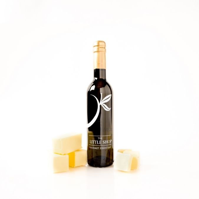 A bottle of gourmet risotto oil with butter cubes arranged around it on a clean white background. The bottle has a dark label with a white leaf graphic and reads 'The Little Shop Gourmet Risotto Oil'.