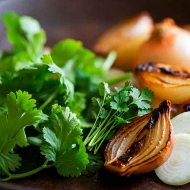 Fresh green cilantro herbs mixed with roasted caramelized onion slices on a dark rustic plate or surface.