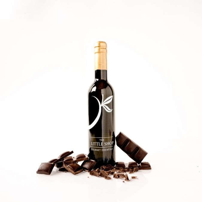 A bottle of gourmet balsamic vinegar with a gold foil top and a black label styled with broken dark chocolate pieces on a white background.