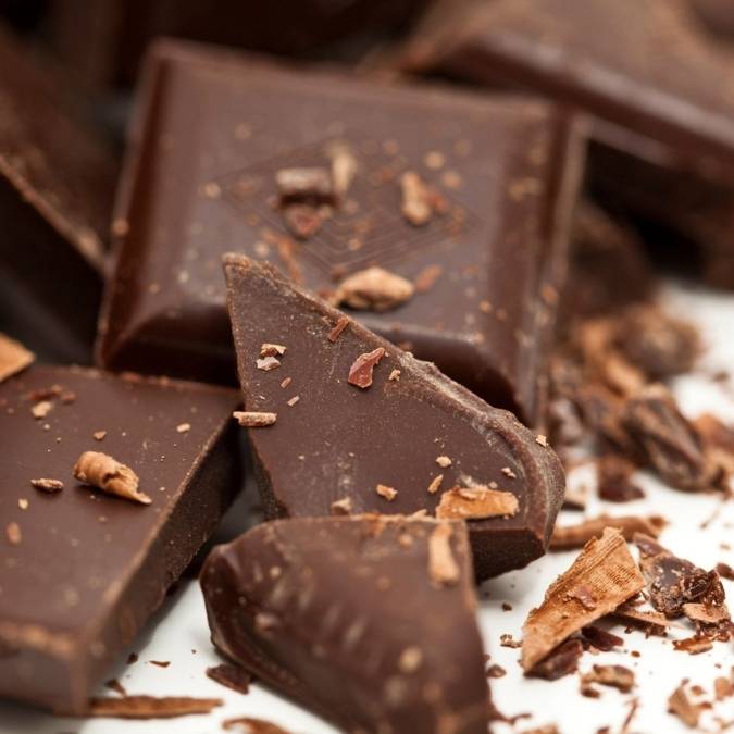 Close-up of several dark chocolate squares and broken pieces with scattered chocolate shavings on a white surface.