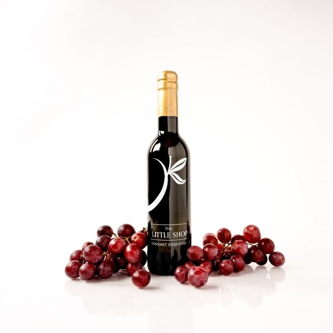 Bottle of Denissimo Dark Balsamic Vinegar with red grapes surrounding the bottle on a white background.