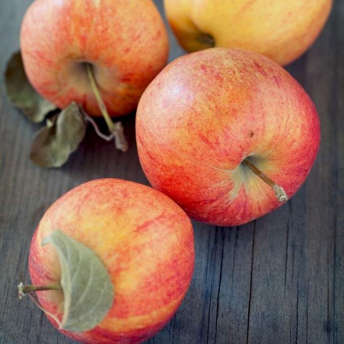 Four red and yellow apples with stems and leaves arranged on a dark wooden surface.