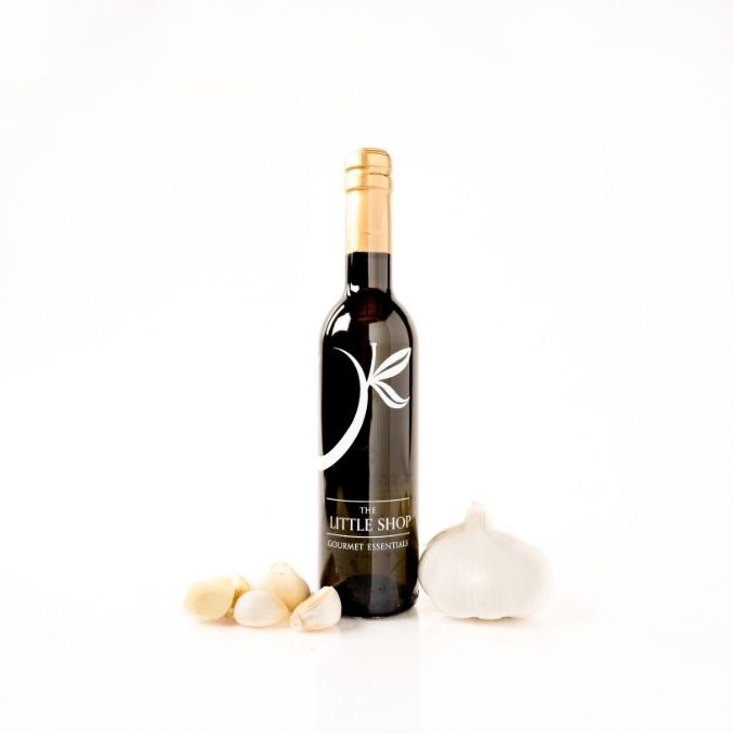 A bottle of gourmet garlic olive oil, styled with fresh garlic cloves and a whole garlic bulb on a clean white background.