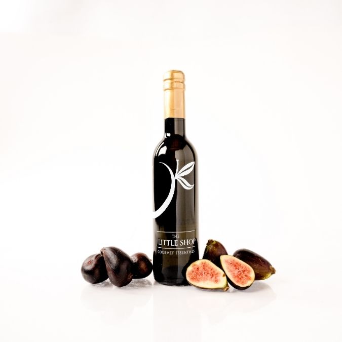 A bottle of Fig Gourmet Essentials by The Little Shop, styled with fresh whole and sliced figs on a clean white background.