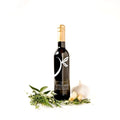 A bottle of gourmet balsamic vinegar from 'The Little Shop' is displayed on a clean white background, styled with fresh herbs, garlic, and a whole garlic bulb.