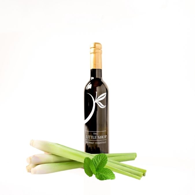 A bottle of gourmet white balsamic vinegar from 'THE LITTLE SHOP' on a clean white background with lemongrass and mint styled around the bottle. 