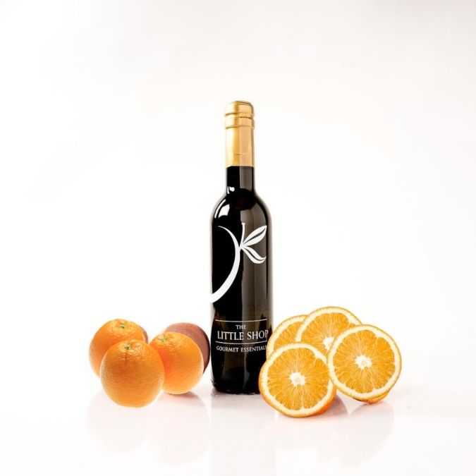 A bottle of Valencia orange olive oil by The Little Shop, styled with whole and sliced oranges on a clean white background.