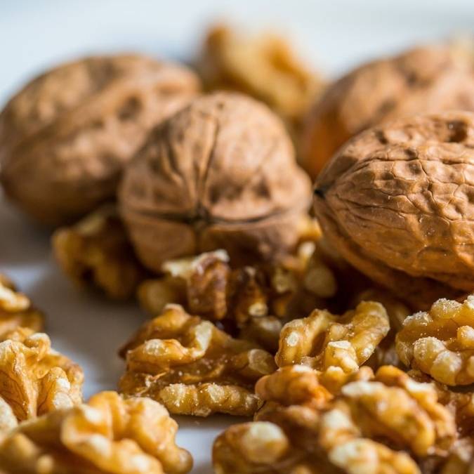 Close-up of whole and cracked walnuts on a light neutral surface, with shallow depth of field focusing on the foreground pieces.